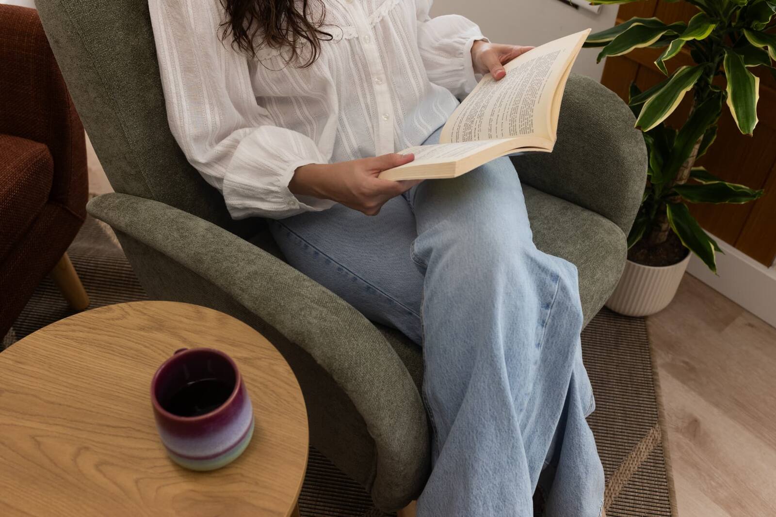 Laia sentada en el sillón de la consulta leyendo un libro, con una taza sobre la mesita